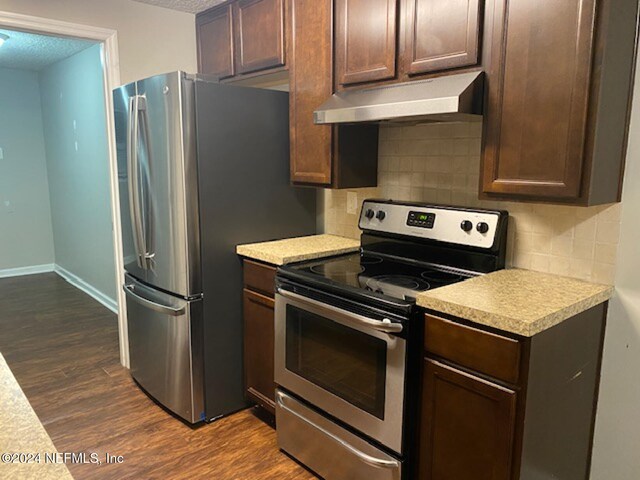 kitchen with a textured ceiling, stainless steel appliances, dark brown cabinets, and dark hardwood / wood-style flooring