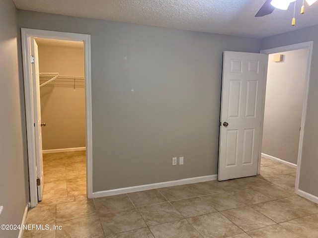 unfurnished bedroom featuring light tile patterned floors, ceiling fan, a textured ceiling, a closet, and a walk in closet