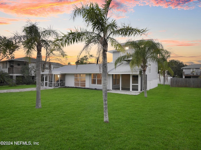 back house at dusk featuring a sunroom and a lawn