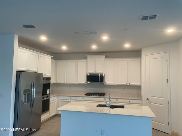 kitchen with sink, appliances with stainless steel finishes, a kitchen island with sink, and white cabinetry