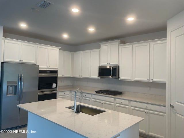 kitchen with sink, white cabinetry, appliances with stainless steel finishes, an island with sink, and light stone countertops