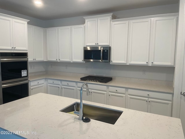 kitchen with stainless steel appliances, light stone countertops, sink, and white cabinets