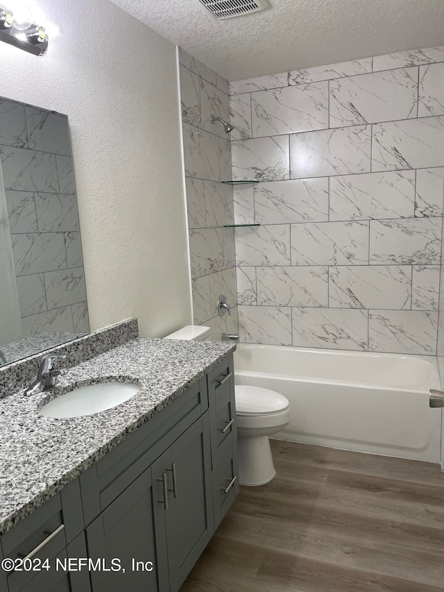 full bathroom featuring toilet, wood-type flooring, tiled shower / bath, vanity, and a textured ceiling