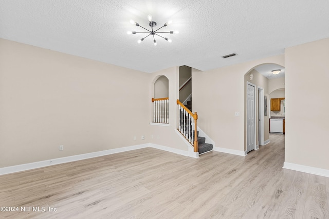 unfurnished room featuring a notable chandelier, a textured ceiling, and light hardwood / wood-style floors