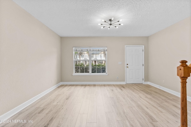 empty room featuring light hardwood / wood-style floors, a notable chandelier, and a textured ceiling