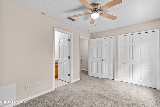 unfurnished bedroom featuring multiple closets, a textured ceiling, light colored carpet, and ceiling fan