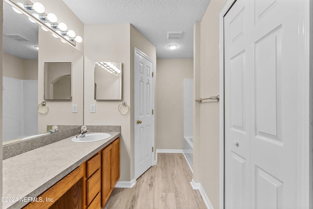 bathroom with vanity, hardwood / wood-style floors, a textured ceiling, and a bathing tub