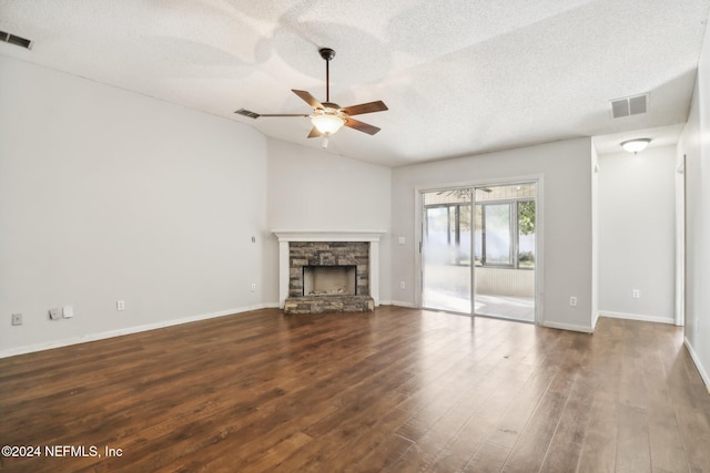 unfurnished living room with a stone fireplace, dark wood-type flooring, a textured ceiling, and ceiling fan