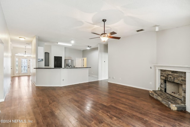 unfurnished living room with a stone fireplace, dark wood-type flooring, and ceiling fan