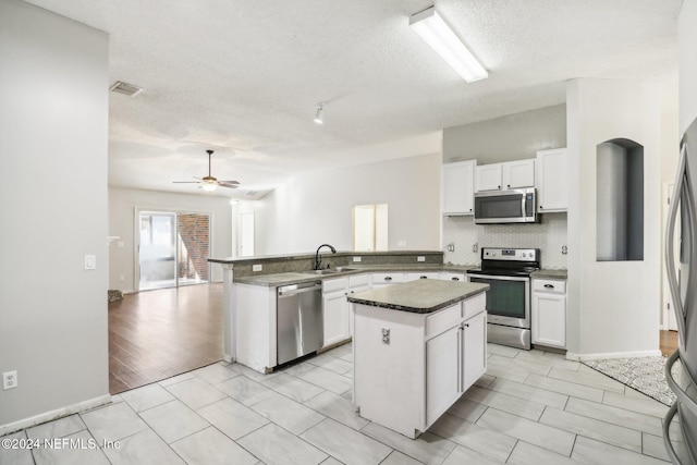 kitchen featuring a textured ceiling, stainless steel appliances, white cabinets, and a kitchen island