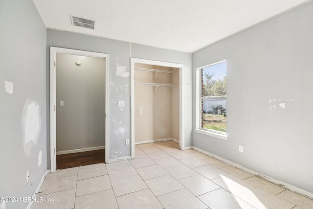 unfurnished bedroom featuring light tile patterned flooring, a closet, multiple windows, and a textured ceiling