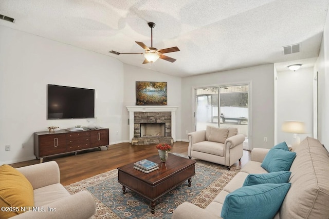 living room featuring lofted ceiling, light hardwood / wood-style flooring, ceiling fan, a textured ceiling, and a stone fireplace