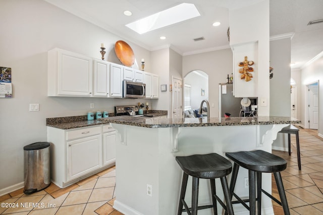 kitchen featuring a skylight, ornamental molding, light tile patterned flooring, white cabinetry, and stainless steel appliances