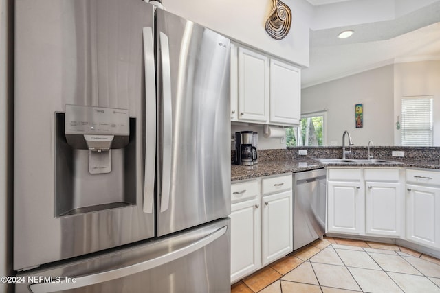 kitchen with sink, stainless steel appliances, light tile patterned floors, dark stone countertops, and white cabinets