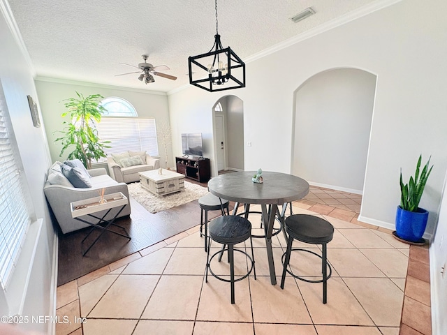 tiled dining area with ceiling fan, a textured ceiling, and ornamental molding