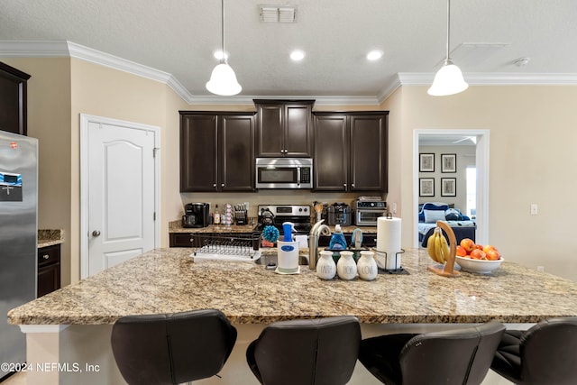 kitchen with an island with sink, a kitchen bar, stainless steel appliances, crown molding, and decorative light fixtures