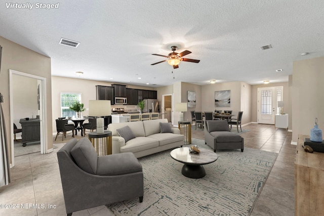 tiled living room featuring ceiling fan, a wealth of natural light, and a textured ceiling