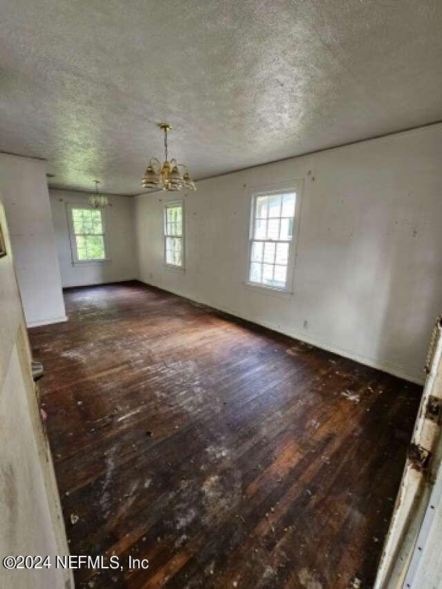 spare room with a textured ceiling, an inviting chandelier, plenty of natural light, and dark hardwood / wood-style floors