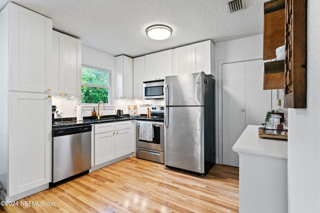 kitchen with white cabinetry, a textured ceiling, light wood-type flooring, sink, and stainless steel appliances