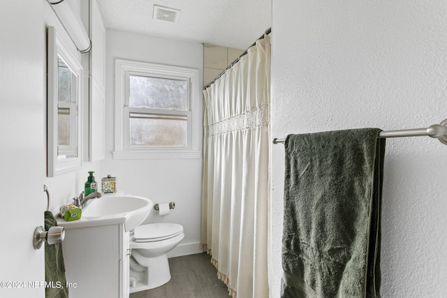 bathroom featuring toilet, a textured ceiling, walk in shower, and vanity