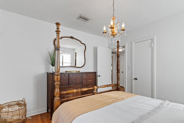 bedroom with hardwood / wood-style floors, a textured ceiling, and a chandelier