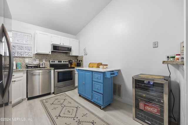 kitchen with appliances with stainless steel finishes, light wood-type flooring, blue cabinets, beverage cooler, and white cabinets