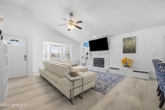 living room featuring high vaulted ceiling, light hardwood / wood-style floors, a stone fireplace, and ceiling fan