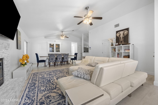 living room featuring ceiling fan, a stone fireplace, lofted ceiling, and light hardwood / wood-style flooring