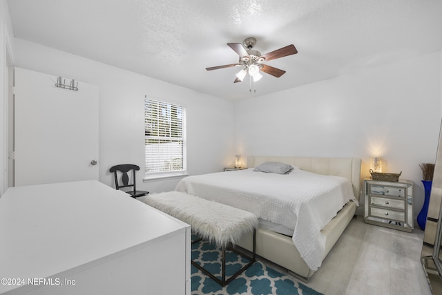 bedroom with ceiling fan, light hardwood / wood-style floors, and a textured ceiling