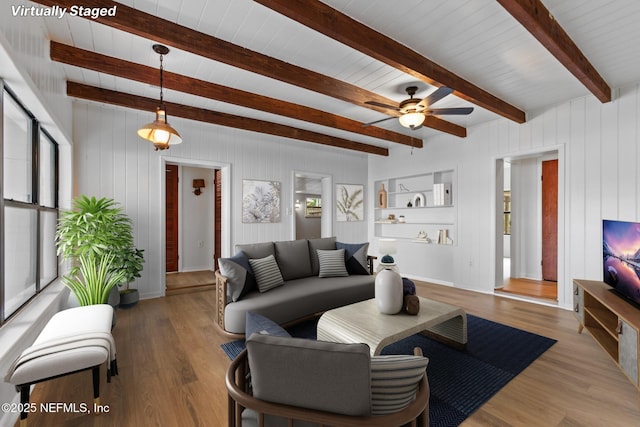 living room featuring beamed ceiling, ceiling fan, wood walls, and wood finished floors
