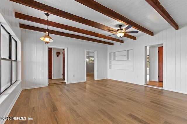 unfurnished living room with baseboards, beam ceiling, a ceiling fan, and wood finished floors