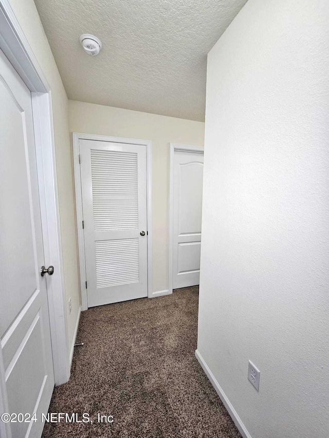 hallway with a textured ceiling and dark carpet