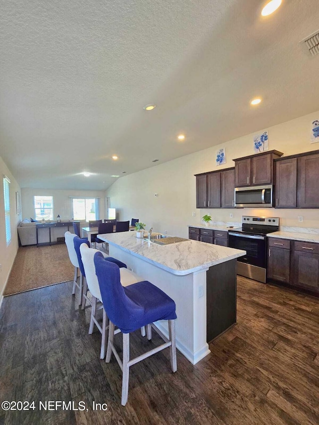 kitchen featuring appliances with stainless steel finishes, dark hardwood / wood-style flooring, a kitchen breakfast bar, light stone counters, and a kitchen island with sink