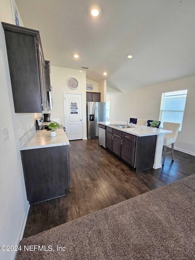 kitchen with dark brown cabinets, an island with sink, appliances with stainless steel finishes, vaulted ceiling, and dark wood-type flooring