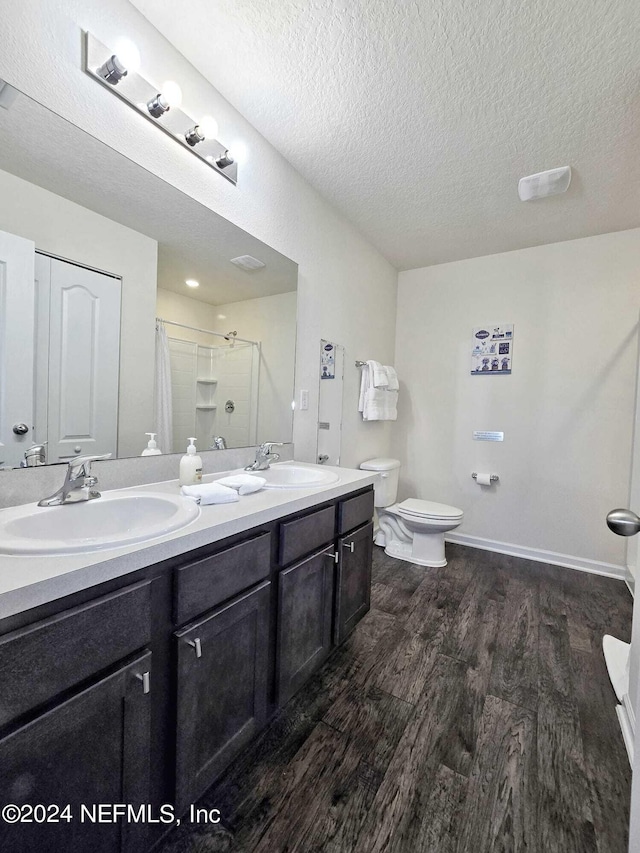 bathroom featuring hardwood / wood-style flooring, toilet, vanity, a textured ceiling, and walk in shower