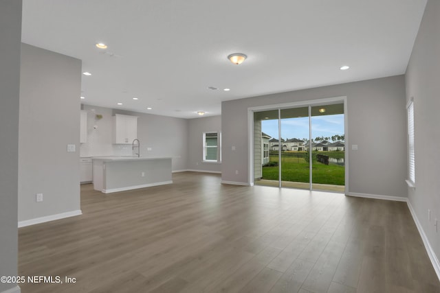 unfurnished living room featuring a sink, baseboards, wood finished floors, and recessed lighting