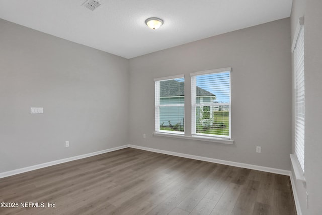 unfurnished room featuring wood finished floors, visible vents, and baseboards