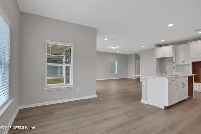 kitchen featuring backsplash, a kitchen island with sink, sink, light hardwood / wood-style flooring, and white cabinetry