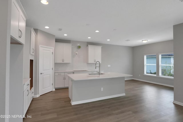 kitchen featuring a center island with sink, dark wood-style floors, a sink, white cabinetry, and backsplash