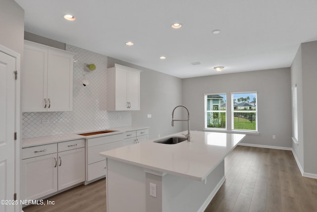 kitchen with tasteful backsplash, white cabinets, an island with sink, light countertops, and a sink