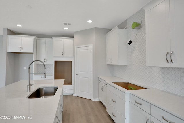 kitchen with light wood finished floors, tasteful backsplash, visible vents, white cabinets, and a sink