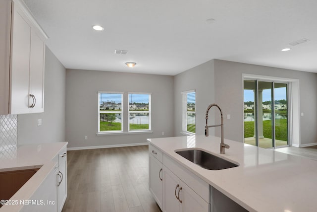 kitchen with light wood-type flooring, white cabinetry, visible vents, and a sink