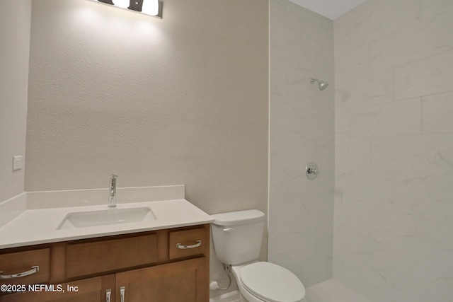 bathroom with a tile shower, vanity, and toilet