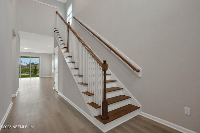 staircase with a high ceiling, baseboards, and wood finished floors