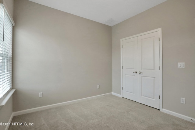 unfurnished bedroom with light carpet, a closet, and baseboards