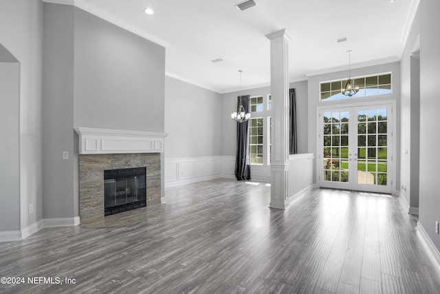 unfurnished living room with hardwood / wood-style flooring, crown molding, ornate columns, a stone fireplace, and french doors