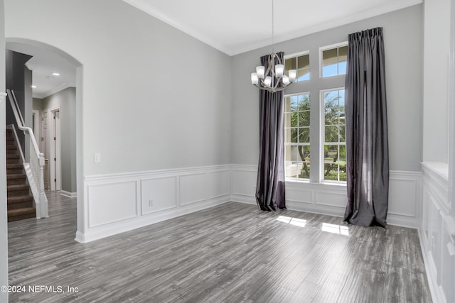 empty room featuring crown molding, wood-type flooring, and an inviting chandelier