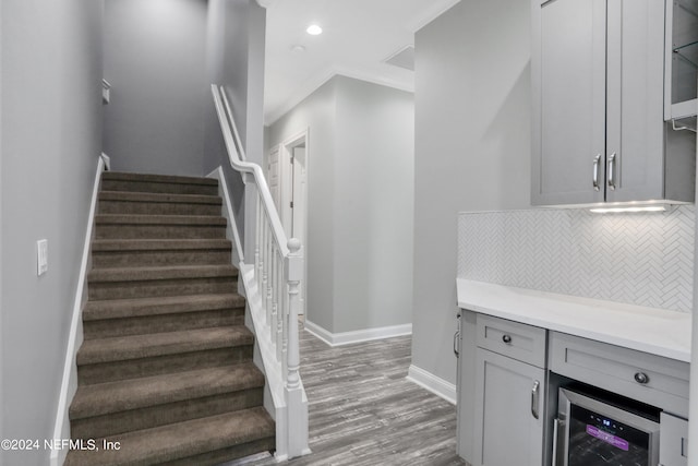 staircase with crown molding, bar area, hardwood / wood-style flooring, and beverage cooler