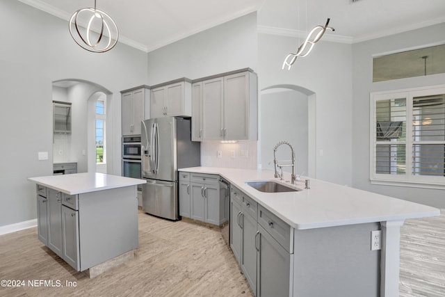 kitchen featuring appliances with stainless steel finishes, sink, an island with sink, light wood-type flooring, and decorative light fixtures