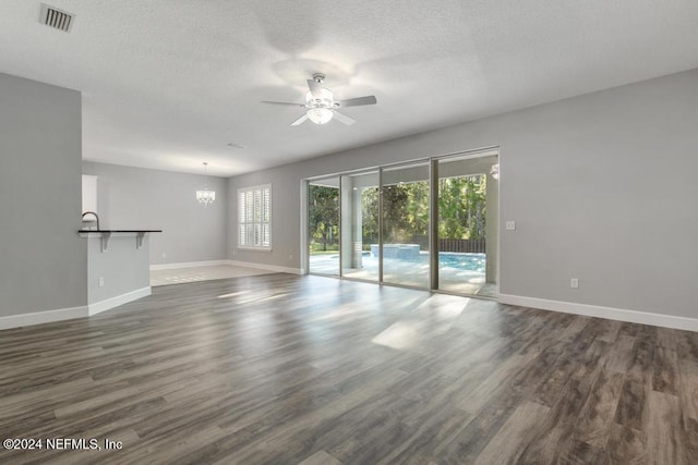 unfurnished living room featuring ceiling fan with notable chandelier, dark hardwood / wood-style floors, and a textured ceiling